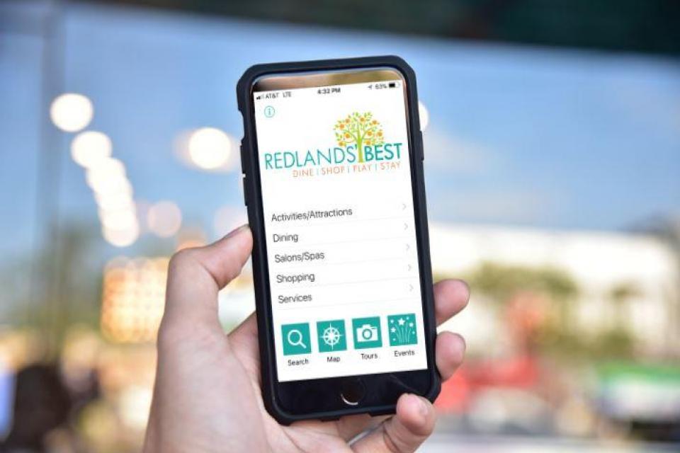 Photo of person holding a mobile phone displaying the Discover Redlands mobile app. 